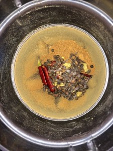 Then add the dry roasted red chilies, pepper, cardamom and cloves together and grind them in the blender.